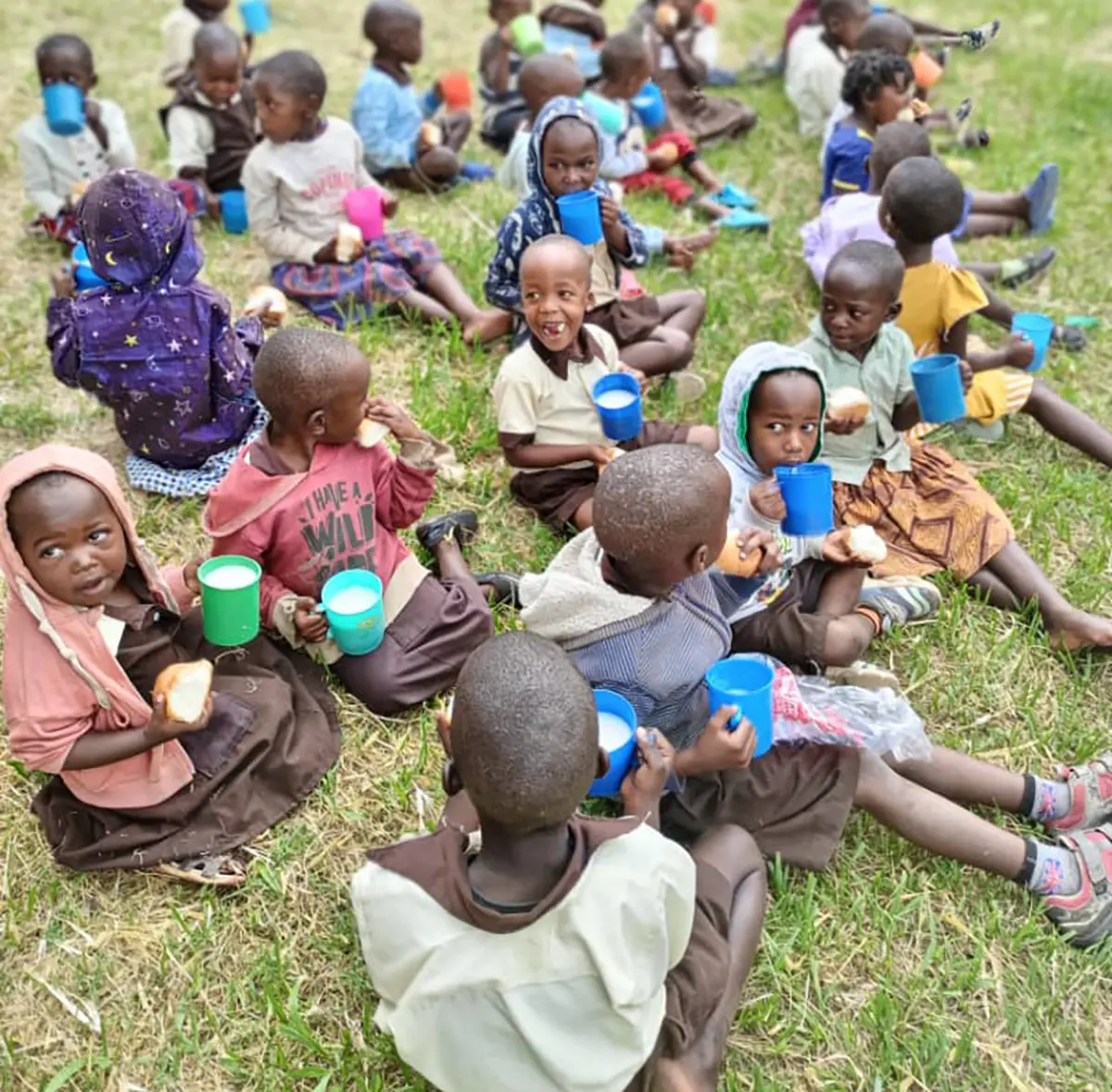 A group of children sat on the ground, smiling and eating breakfast